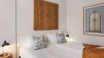 A bedroom with a bed, pillows, a nightstand, a lamp, and a wall-mounted artwork.