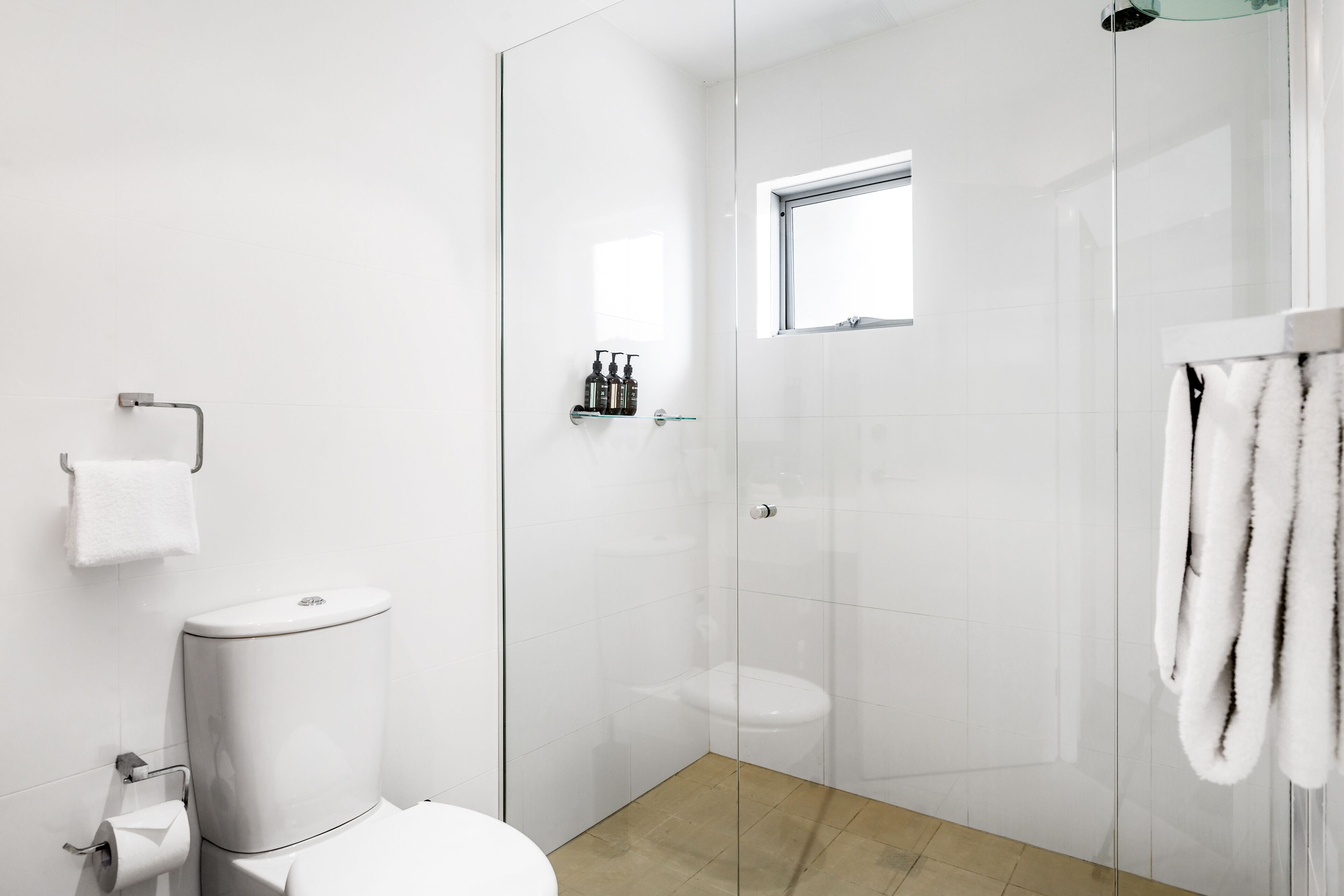 A modern bathroom with a toilet, a glass shower enclosure, and a towel rack.