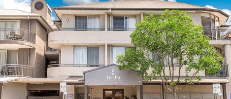 A hotel with a modern design, featuring a central entrance, balconies, and a parking area.