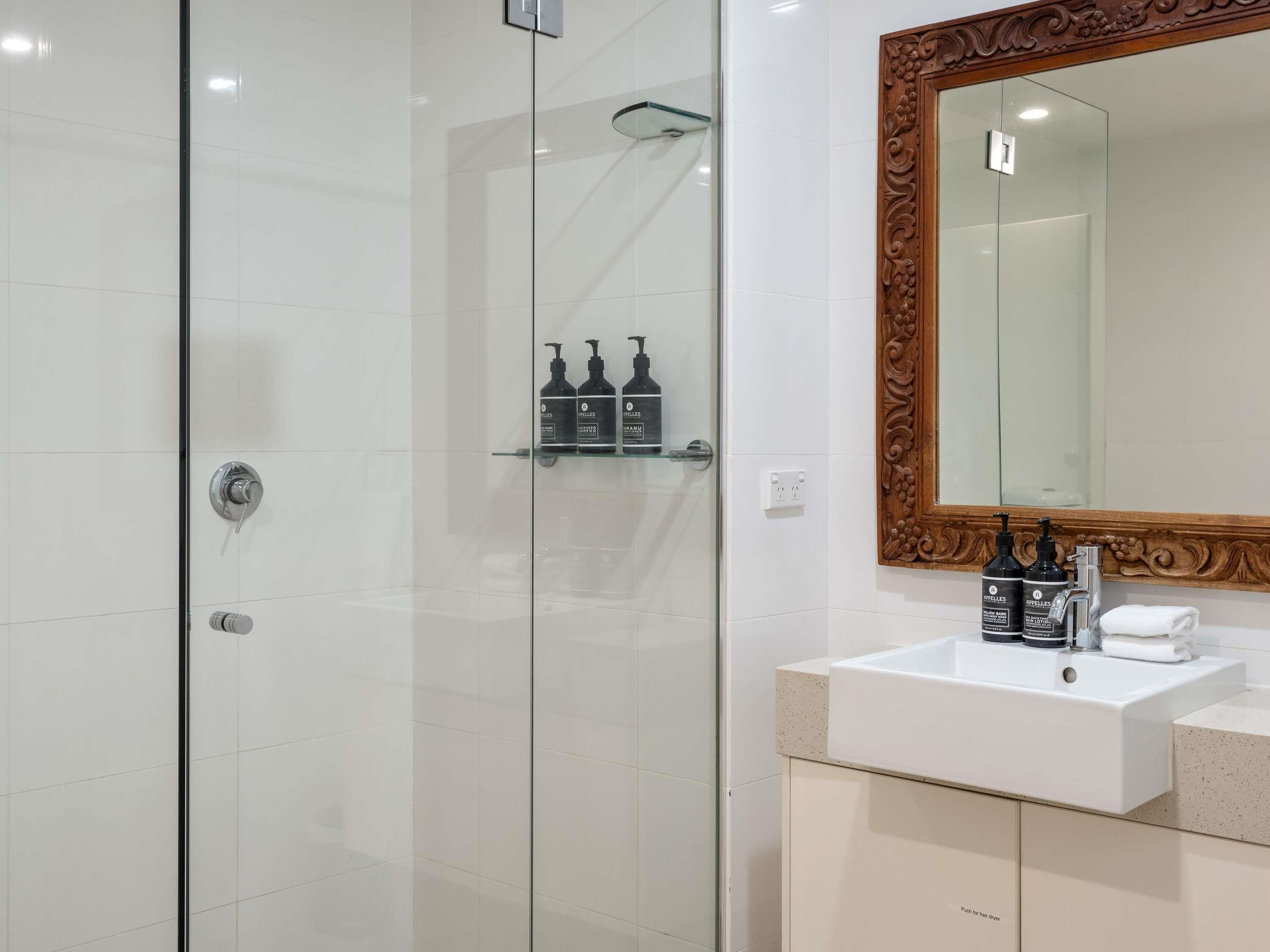 A modern bathroom with a glass shower enclosure, a white sink with a mirror, and toiletries on the wall.