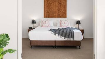 A bed with a brown headboard, white bedding, and decorative pillows. There is a wall-mounted artwork above the bed.