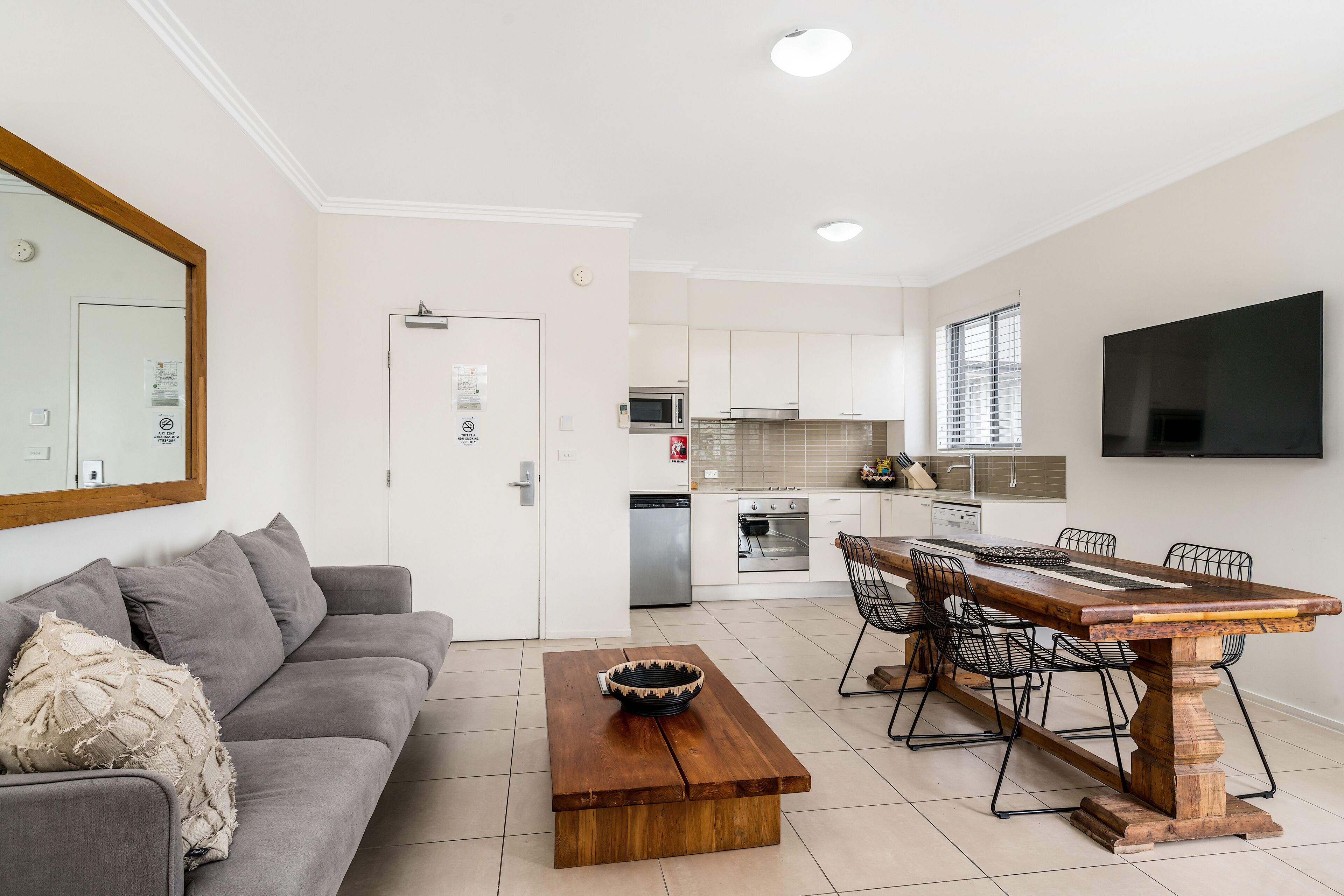 A modern living room with a grey sofa, a wooden coffee table, and a dining area with a wooden table and chairs.