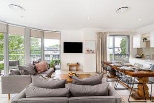 Un salon moderne avec un canapé gris, une table à manger dressée pour six personnes et un téléviseur fixé au mur.
