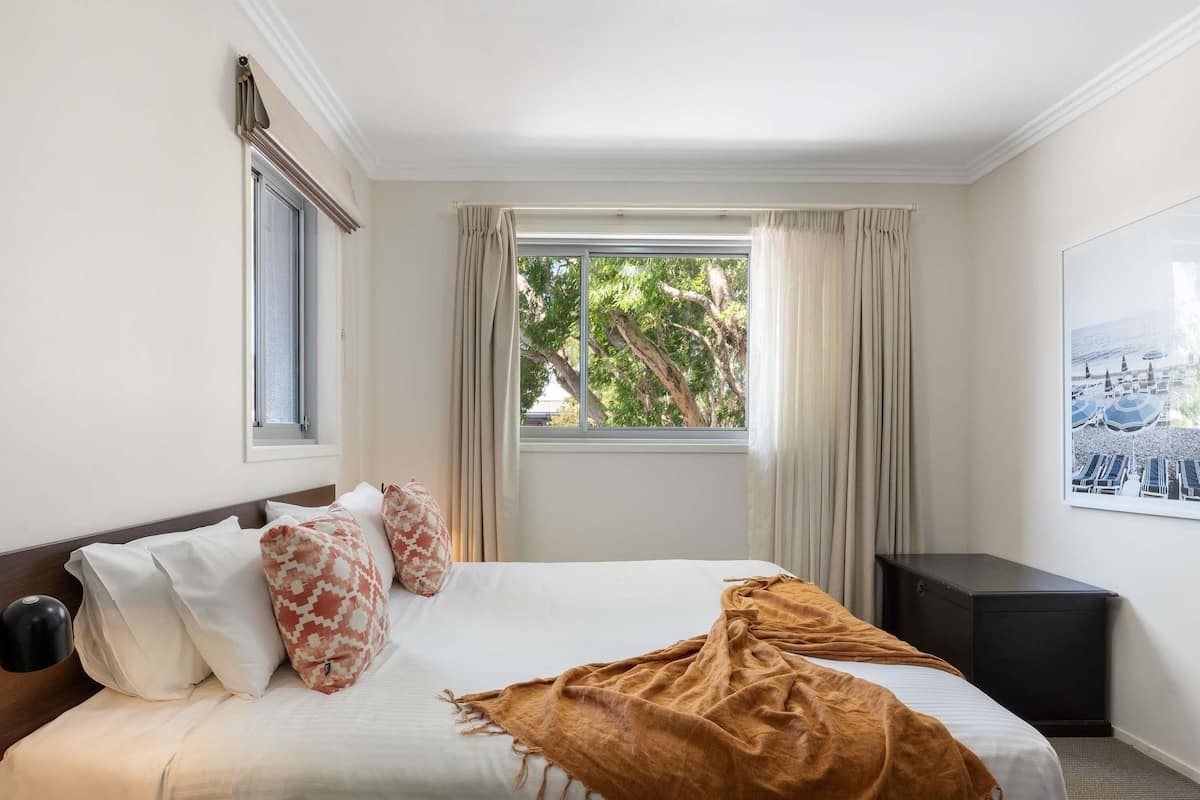 A hotel room with a bed, a window with curtains, a bedside table, and a wall-mounted picture.