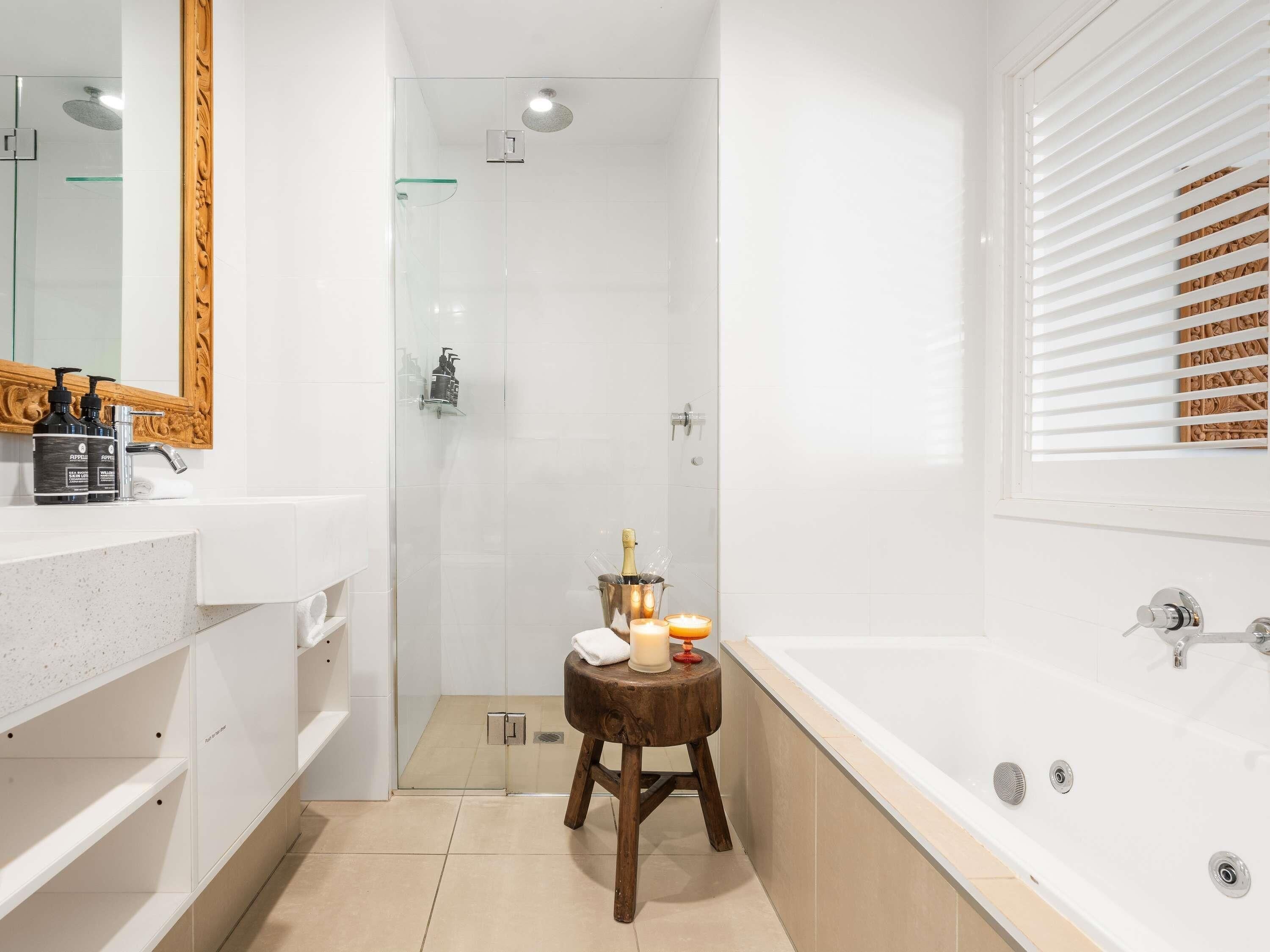 Une salle de bain moderne avec une douche à parois de verre, un tabouret en bois orné de bougies et une grande baignoire.