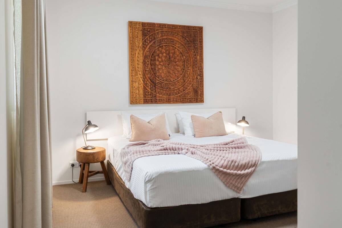 A bedroom with a large bed, two bedside tables, a wall-mounted artwork, and a carpeted floor.