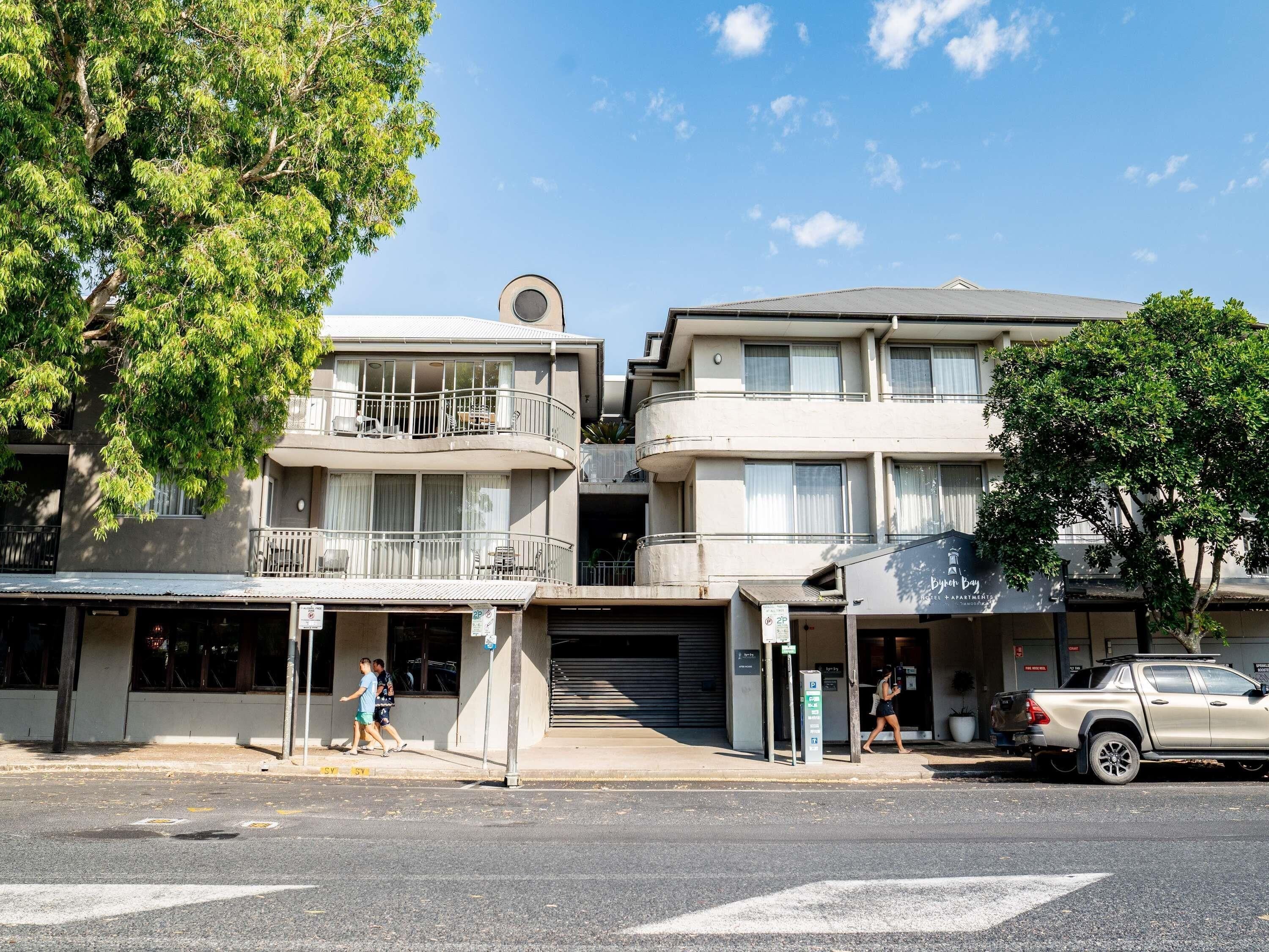 A multi-story building with balconies and a parking area.