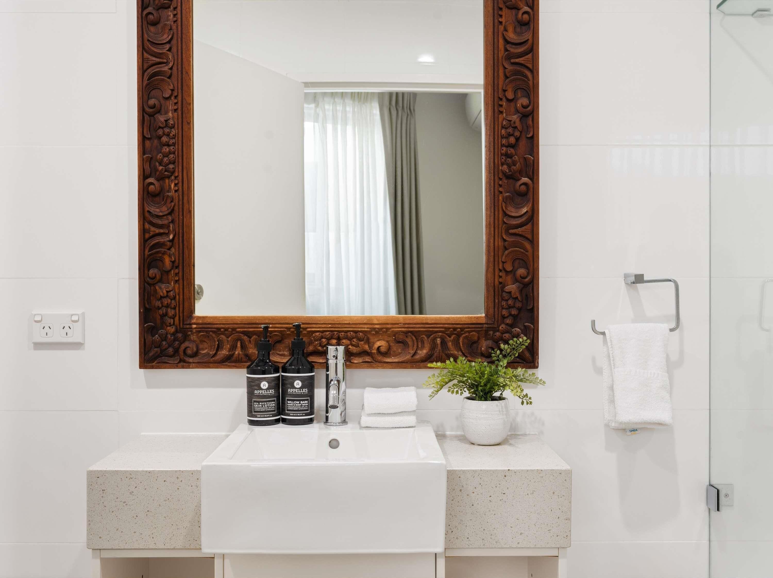 A bathroom with a white sink, two bottles of lotion, a potted plant, and a towel rack.