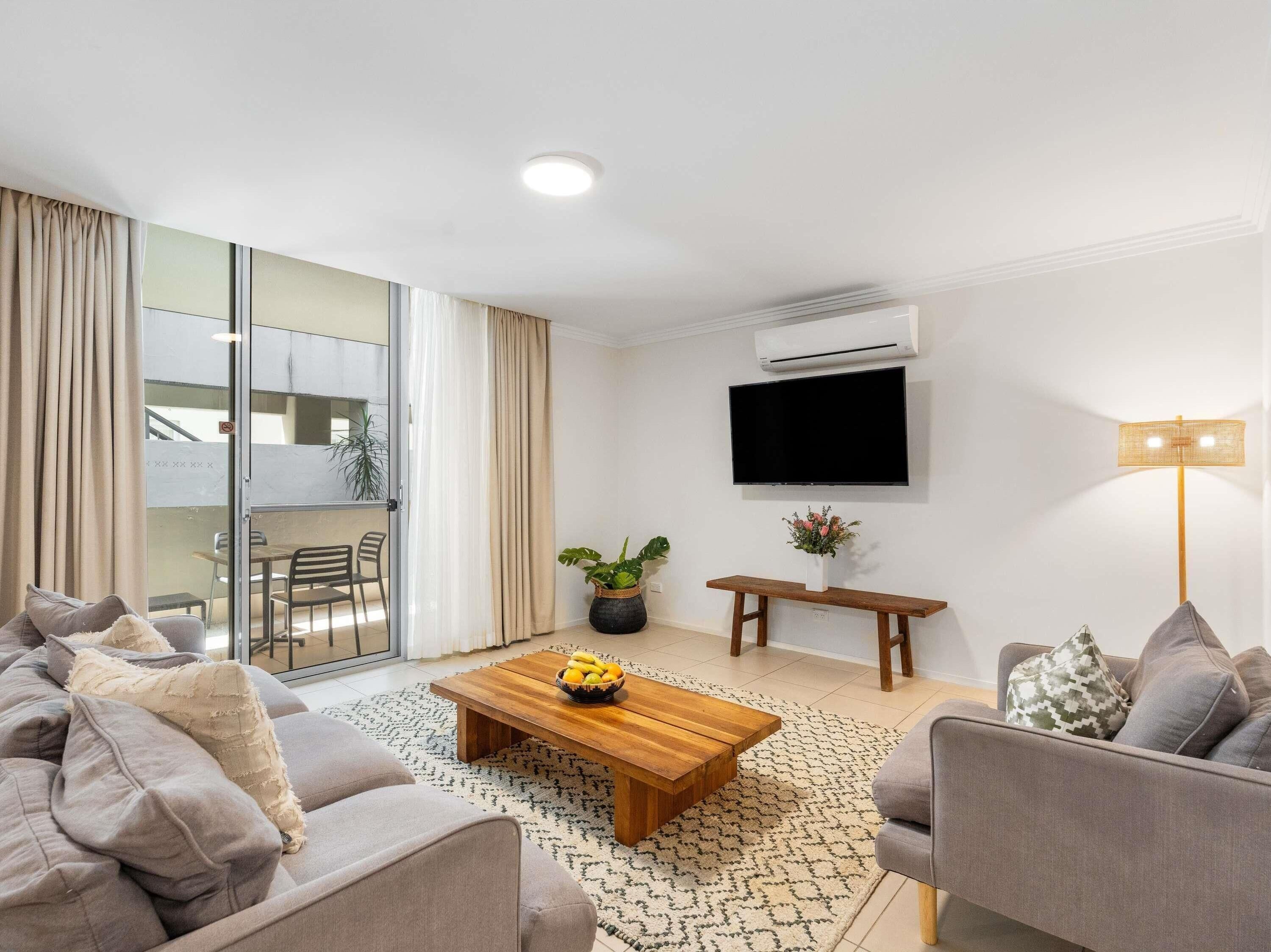 Un salon moderne avec un canapé, une table basse, un téléviseur et un balcon doté de portes vitrées.