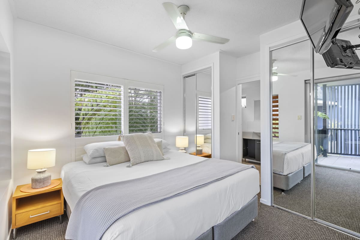A modern hotel room with a large bed, bedside tables with lamps, a ceiling fan, and a large mirror.