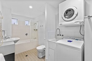 A modern bathroom with a bathtub, toilet, and a built-in washing machine. - Verano Resort (Noosaville)