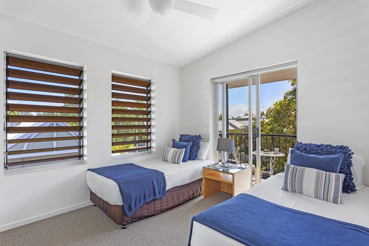 A bedroom with two beds, a balcony, and a view of the outdoors.
