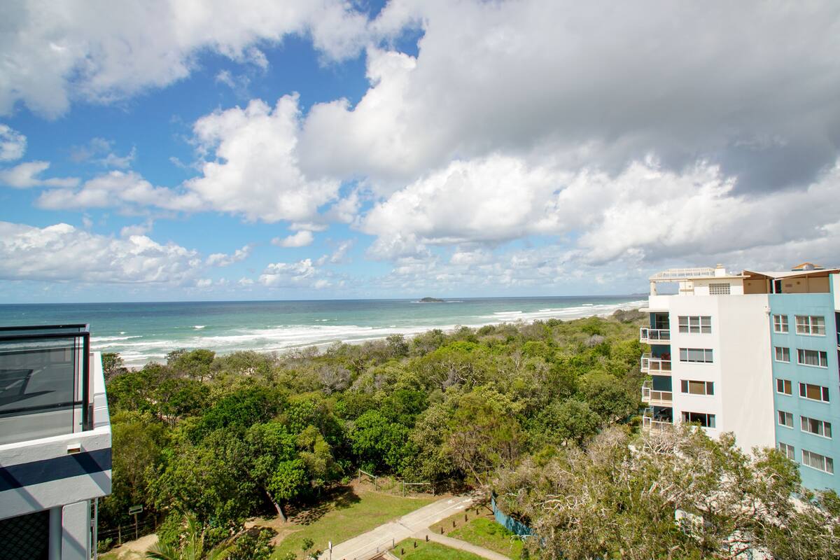 A coastal view with a building overlooking the ocean, surrounded by greenery.