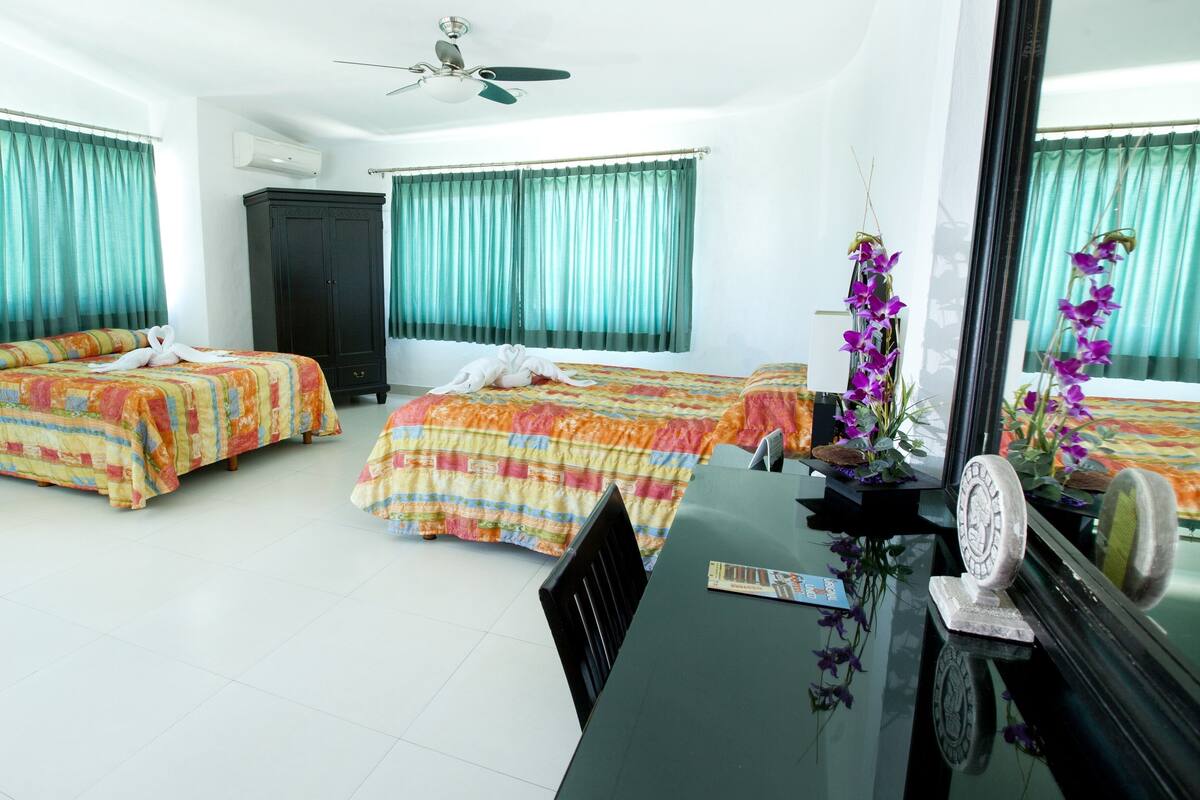 A hotel room with two beds, a desk, a chair, a ceiling fan, and a large mirror.
