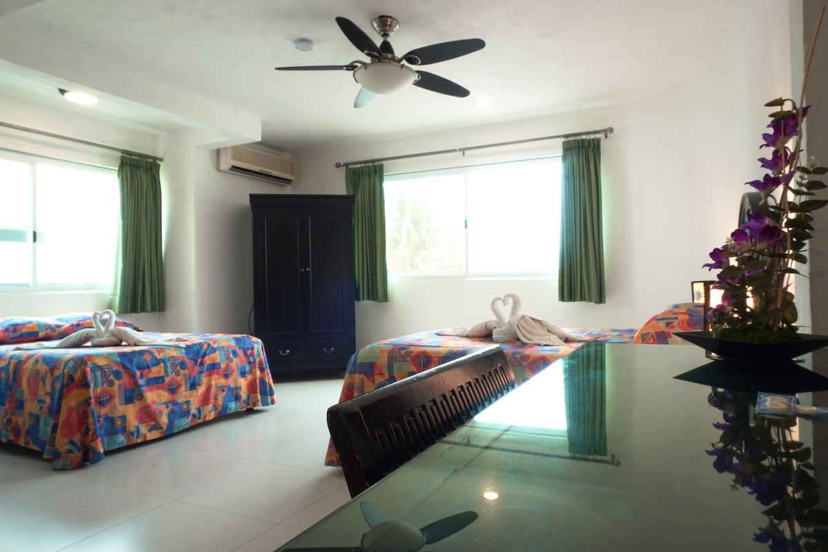 A hotel room with two beds, a ceiling fan, an air conditioning unit, and a window with curtains.