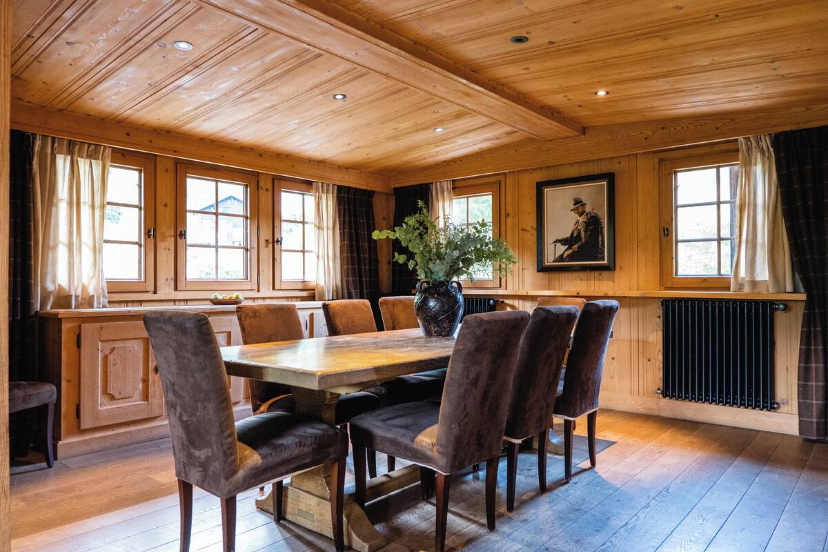 A wooden-paneled dining room with a large table, six chairs, and a potted plant.