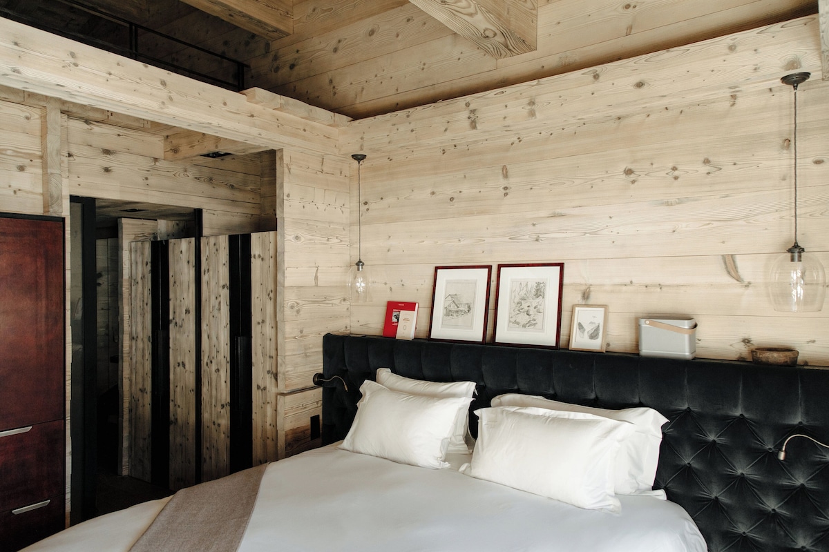 A wooden-paneled bedroom with a tufted headboard, a bed with white linens, and framed artwork on the wall.