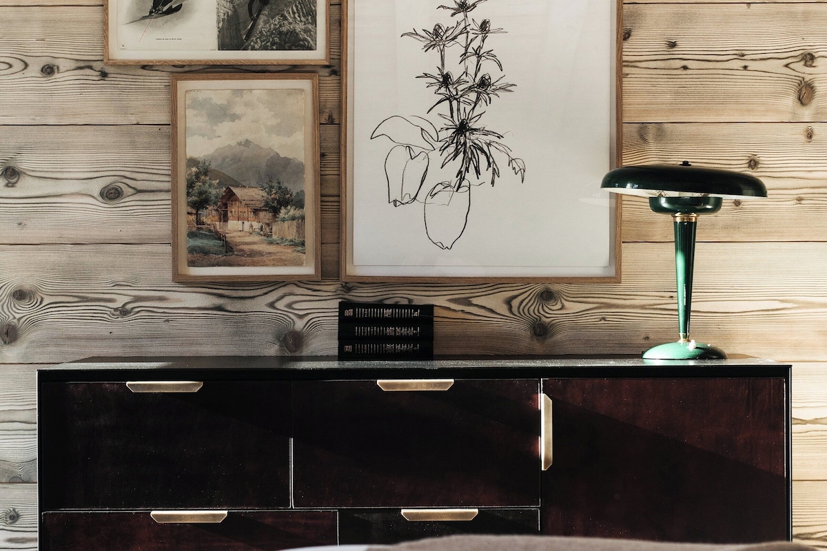 A wooden wall with framed artwork and a teal desk lamp.