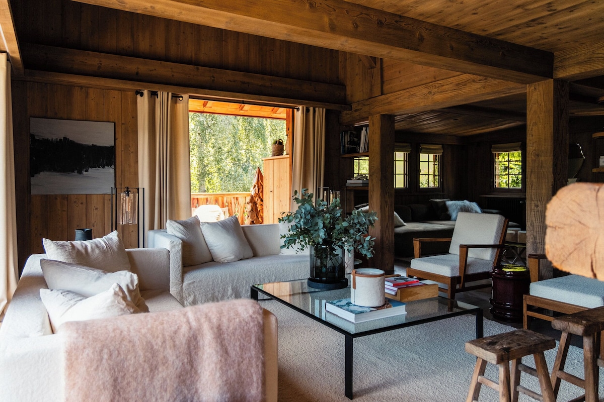 A cozy cabin interior with a sofa, chairs, a coffee table, and a bookshelf.