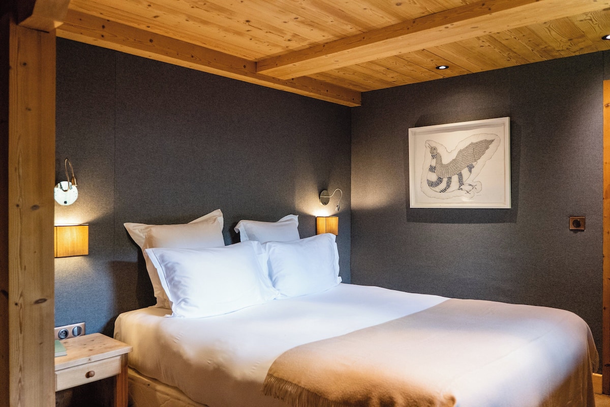 A bedroom with a wooden ceiling, a bed with white linens, two wall-mounted lamps, and a framed picture of an eagle.