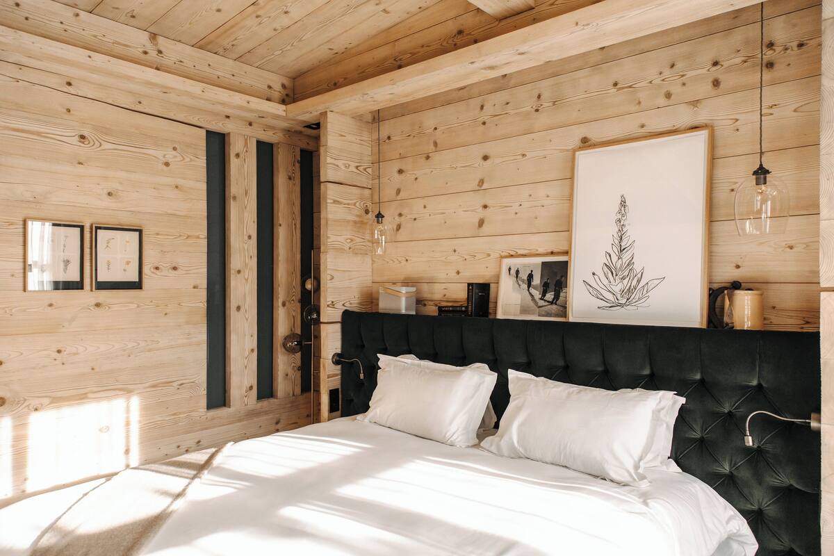 A wooden-paneled room with a bed, framed artwork, and a pendant light.