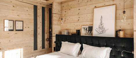 Habitación con paneles de madera, una cama, obras de arte enmarcadas y una lámpara colgante.