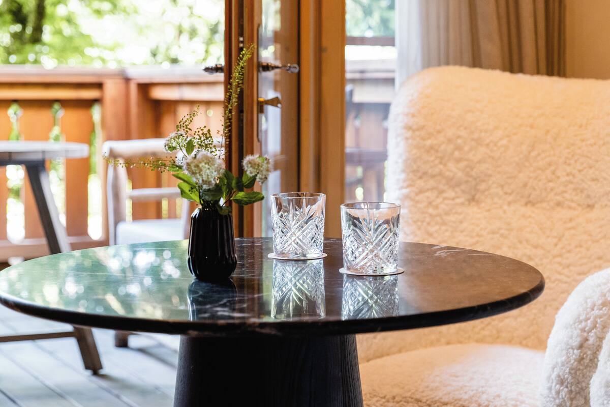 A round glass table with a black base, a vase with flowers, and two clear glass cups.