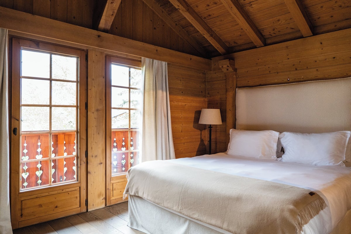 A wooden cabin room with a bed, a nightstand, and a window with curtains.