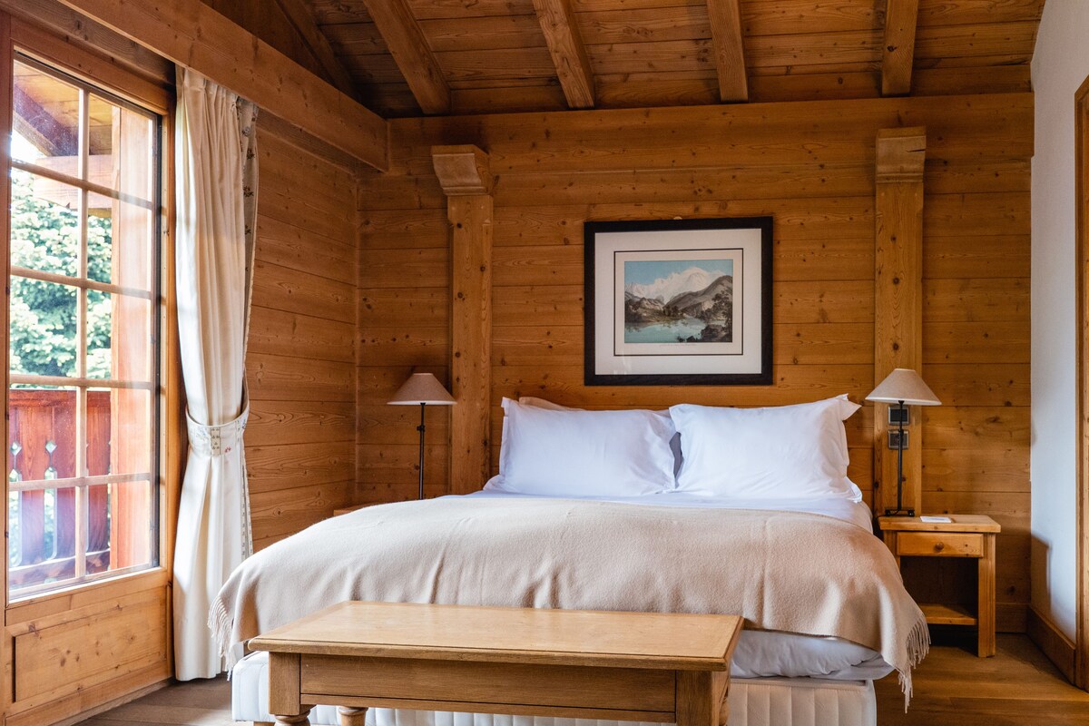A wooden cabin room with a bed, a table, and a window with curtains.