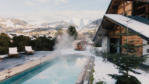 Une cabane en bois avec une piscine, entourée de collines et de montagnes recouvertes de neige.