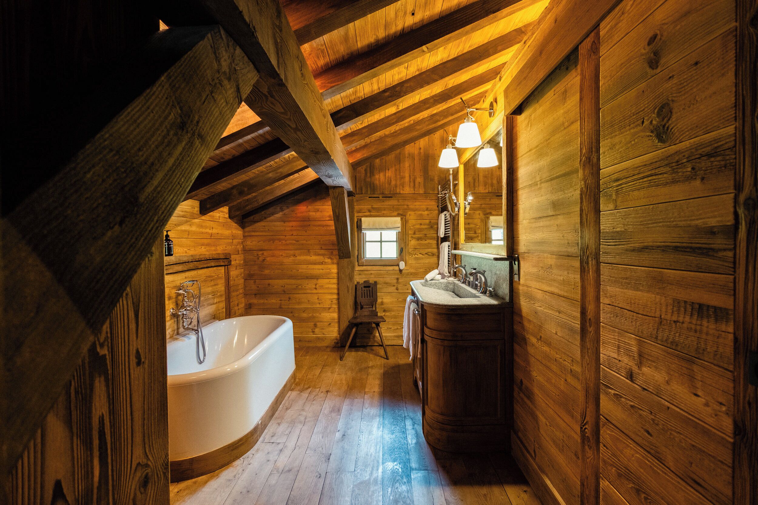 Baño de cabaña de madera con bañera, tocador y ventana.