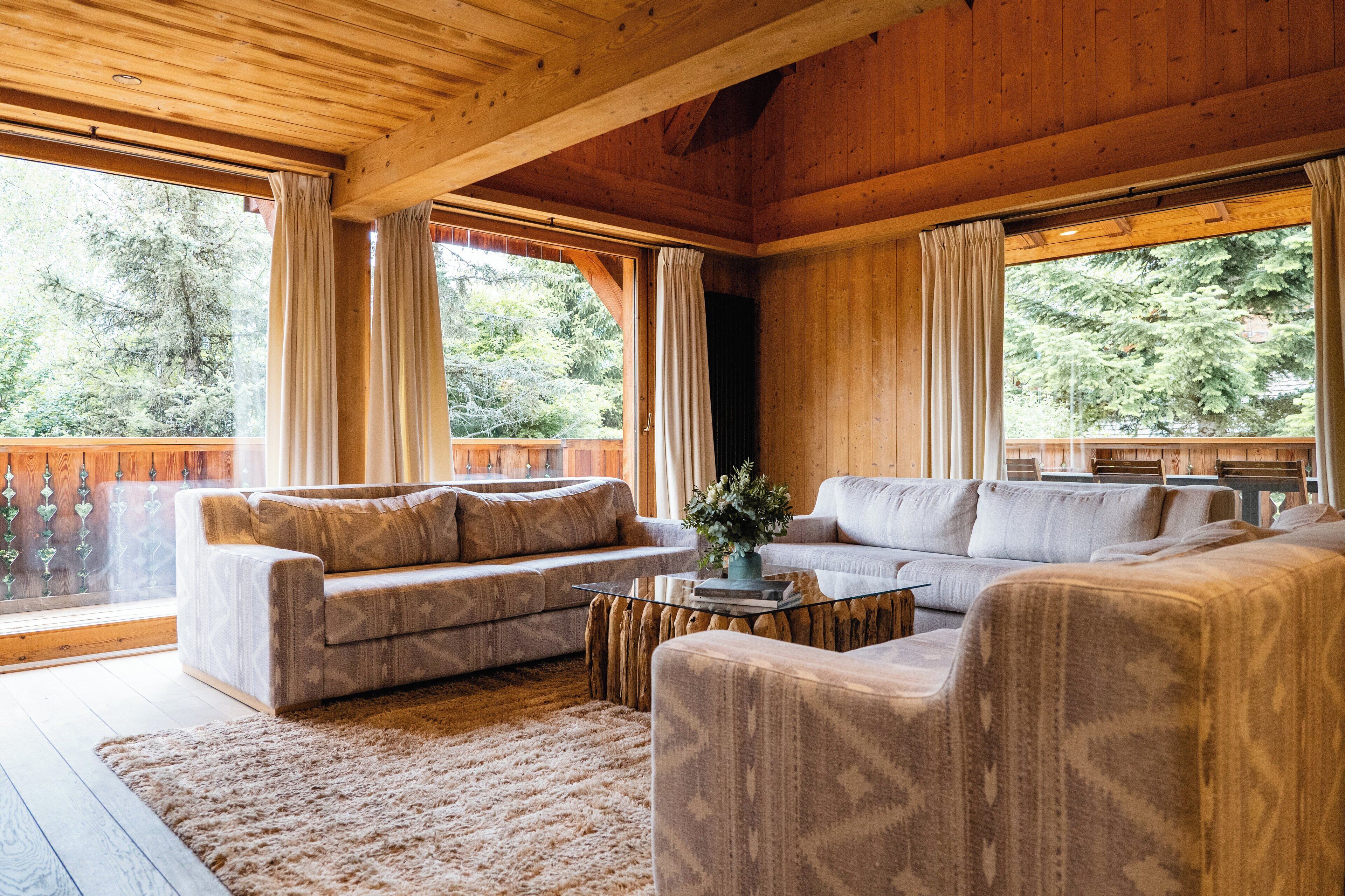 Ein Holzblock-Innenraum mit zwei Sofas, einem Couchtisch und Blick auf einen Wald durch große Fenster.