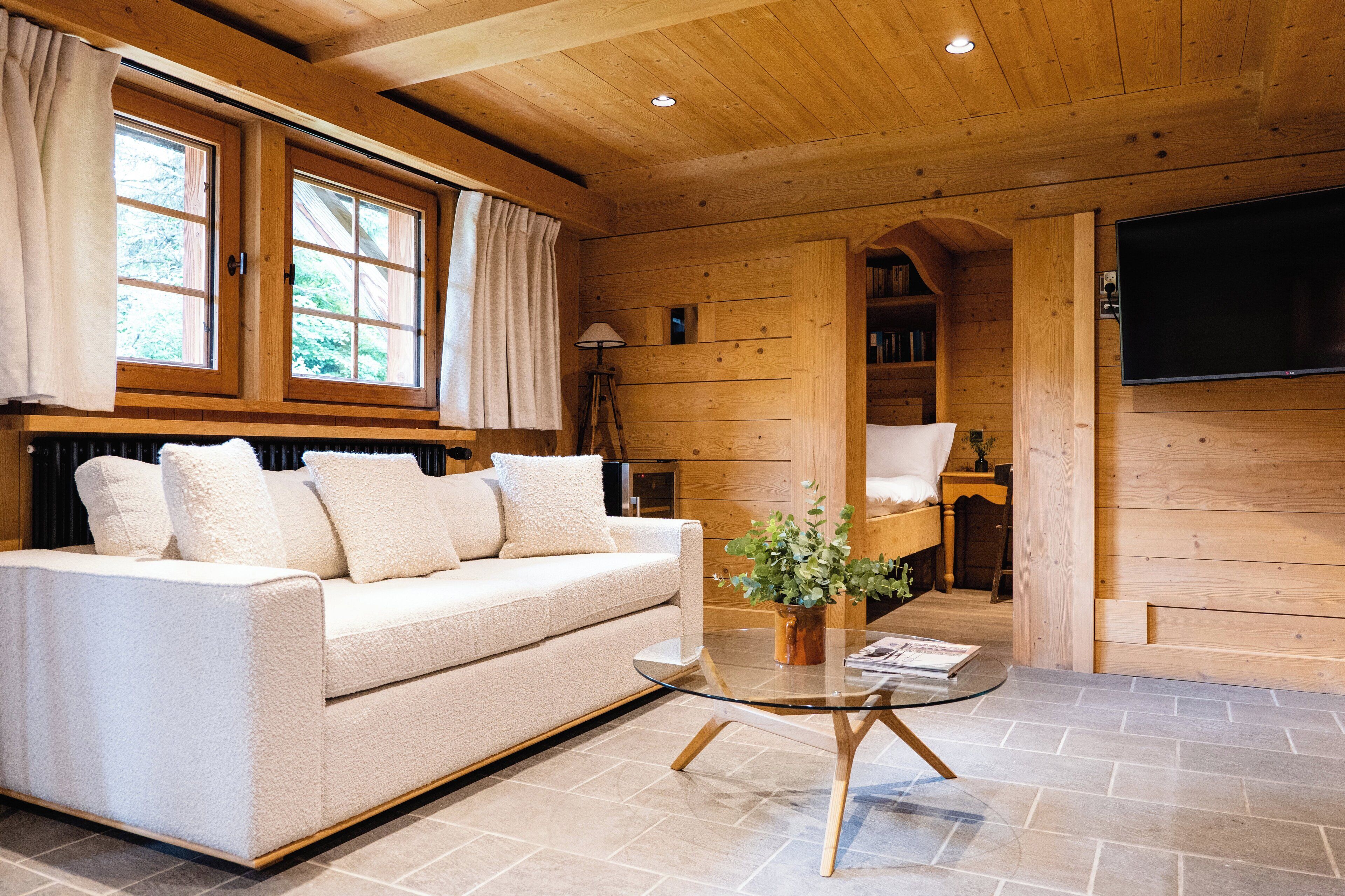 A cozy cabin interior with a sofa, a glass coffee table, a lamp, and a TV mounted on the wall.