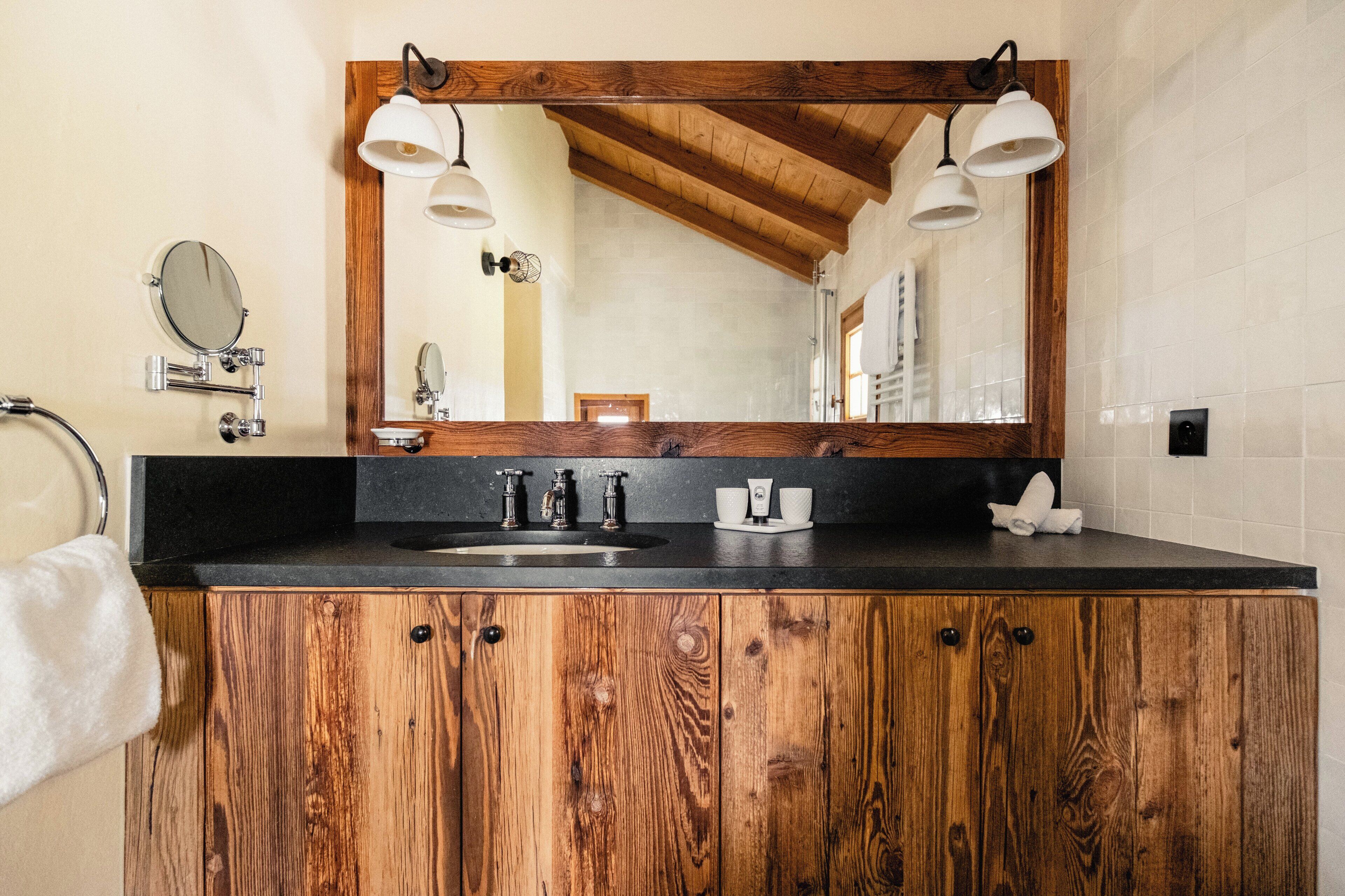 Un baño con tocador de madera, un espejo grande, dos luces empotradas en la pared, un perchero para toallas y un lavabo.
