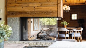 L’intérieur chaleureux d’un chalet avec une cheminée en pierre, un plafond en bois et un coin repas comprenant des chaises et une table.