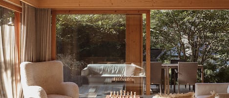 A cozy room with a large window, a comfortable chair, a small table with a chessboard, and wicker furniture.