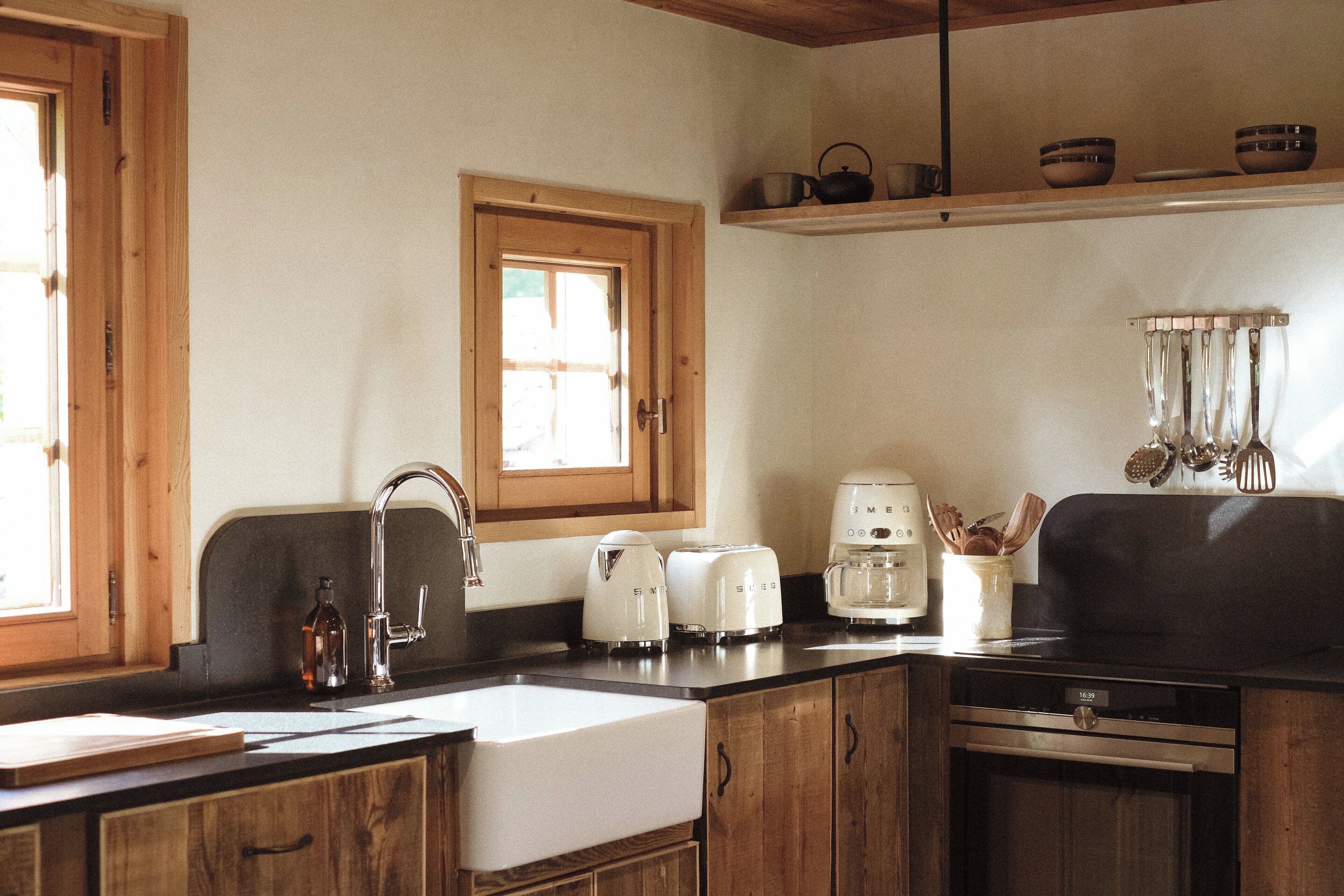 Een keuken met houten kastjes, een spoelbak, een raam en een aanrecht met keukenapparatuur.