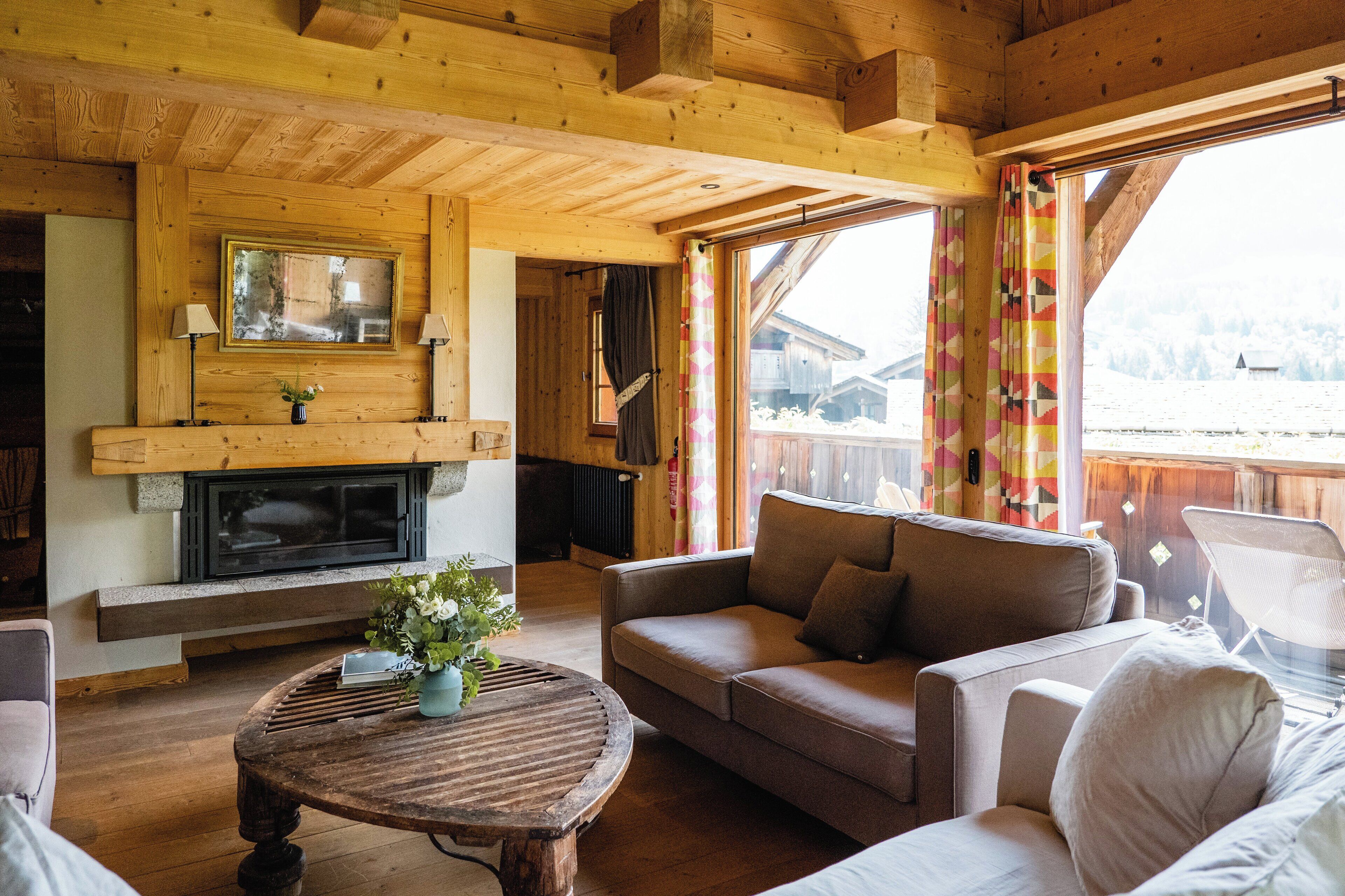 Interior acogedor de una cabaña con chimenea, muebles de madera y vistas a un paisaje nevado.