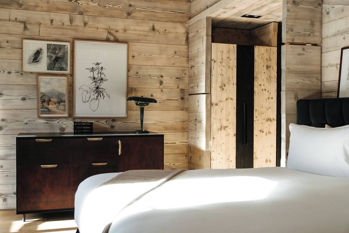 A bedroom with a wooden wall, a bed, a dresser, and framed artwork.