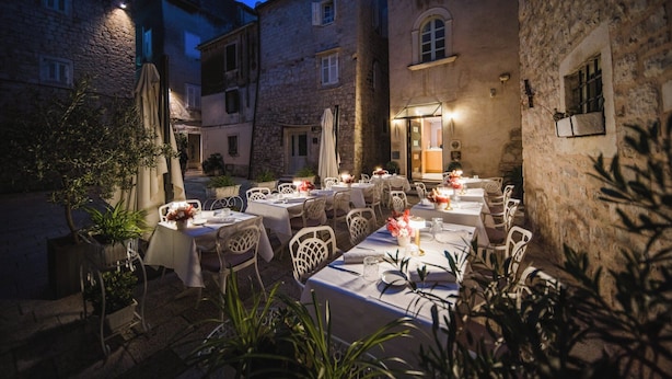 Un área de comedor al aire libre con mesas y sillas, rodeada de edificios de piedra.