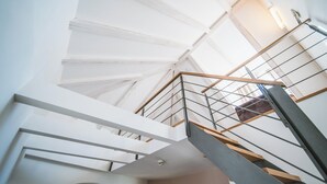 Un interior moderno con una escalera que sube, paredes blancas y un techo con tragaluces.