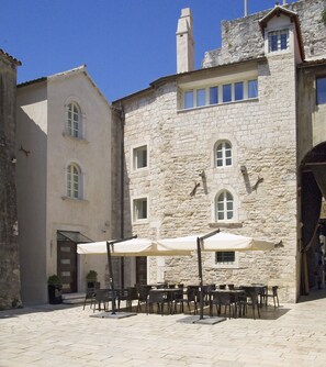 An outdoor café area with stone buildings, tables, and chairs. - Hotel Vestibul Palace (Split)