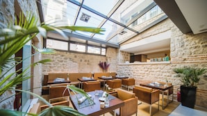 Un restaurante moderno con pared de piedra y techo de vidrio, con mesas y sillas de madera, y plantas en macetas.