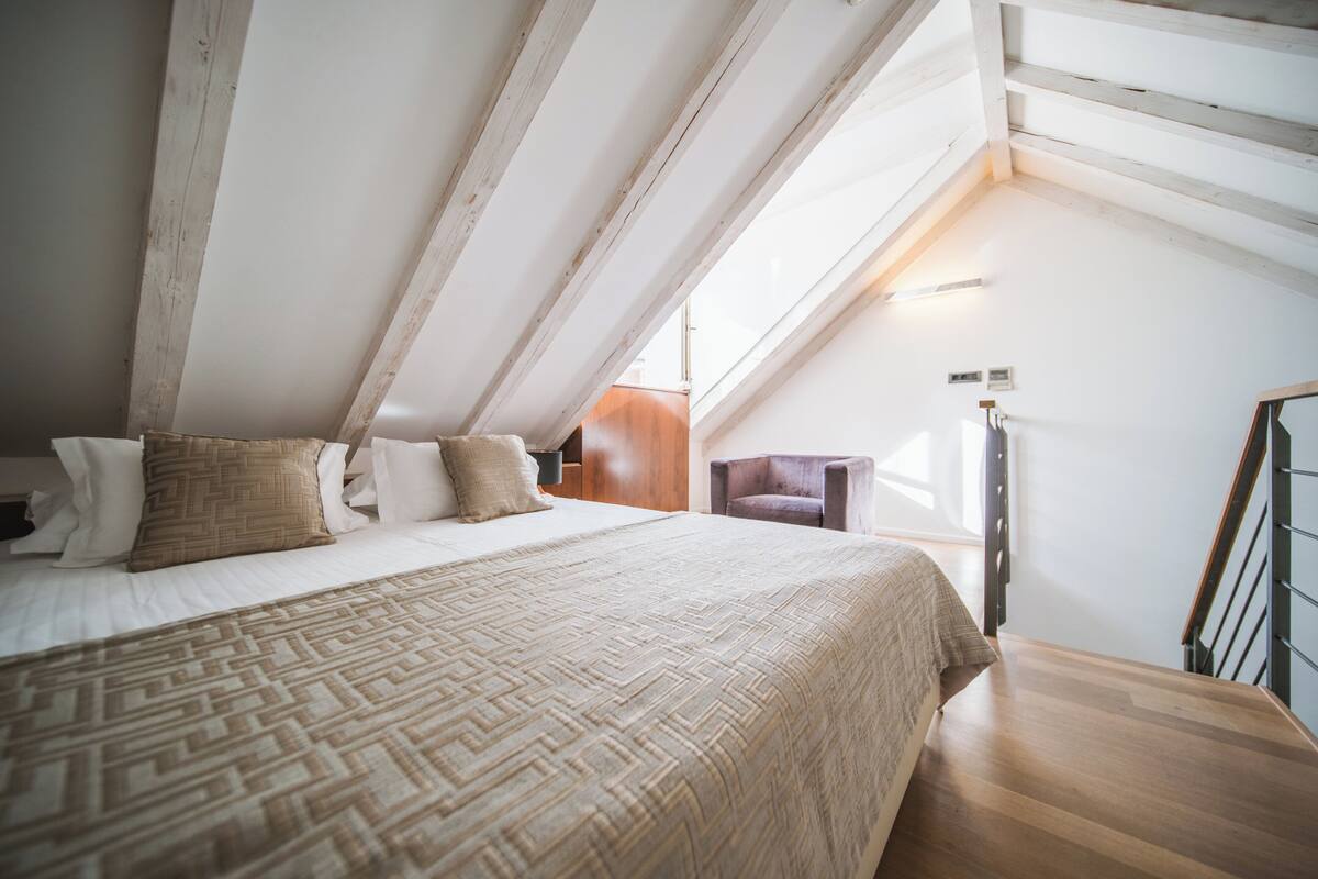 A bedroom with a large bed, a wooden headboard, a window, and a staircase.