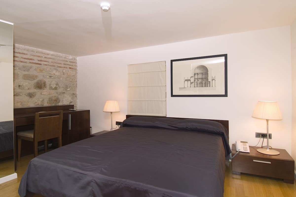 A hotel room with a bed, desk, chair, and a lamp.