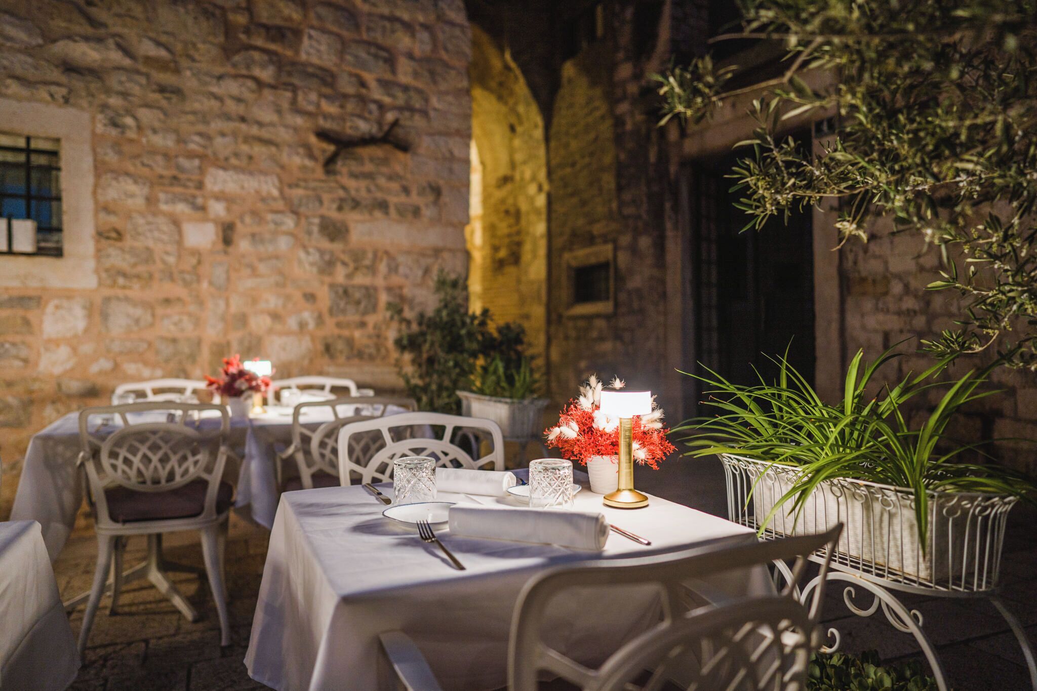 Un área de comedor al aire libre con paredes de piedra, mesas y sillas blancas.