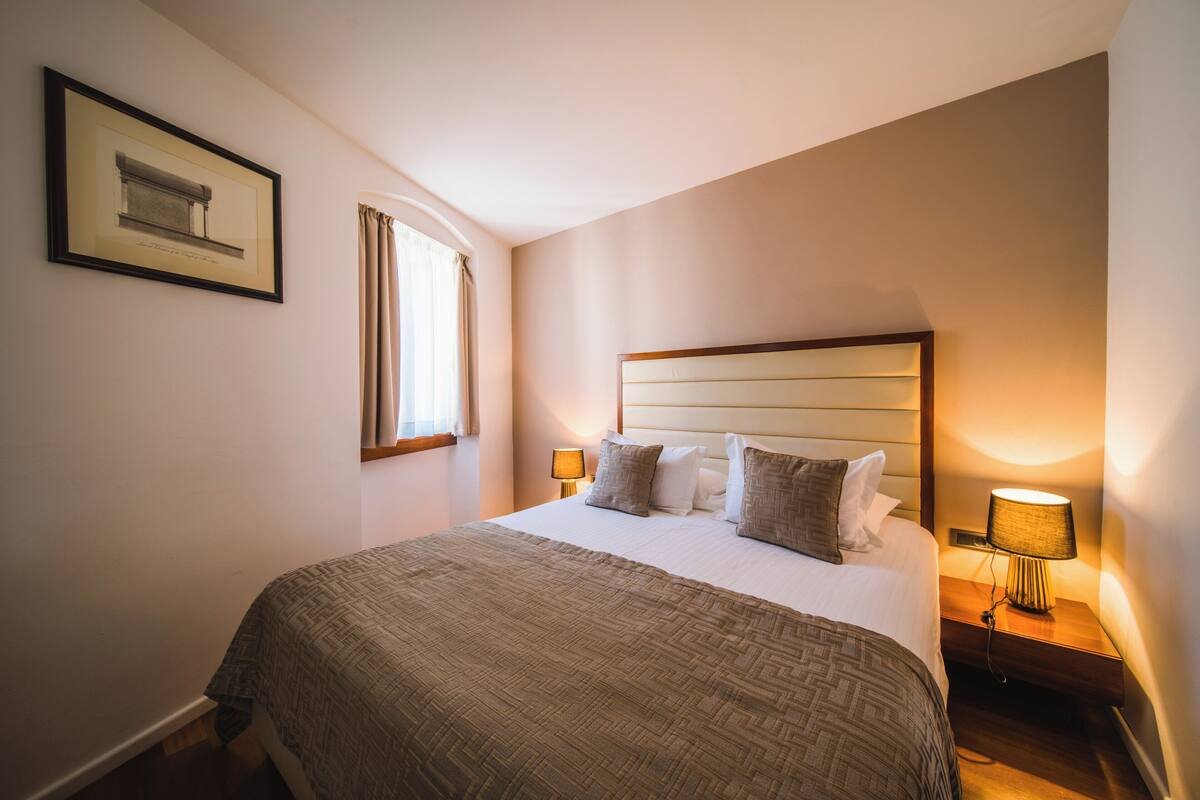 A neatly made bed with a patterned bedspread, a headboard, and two bedside lamps.