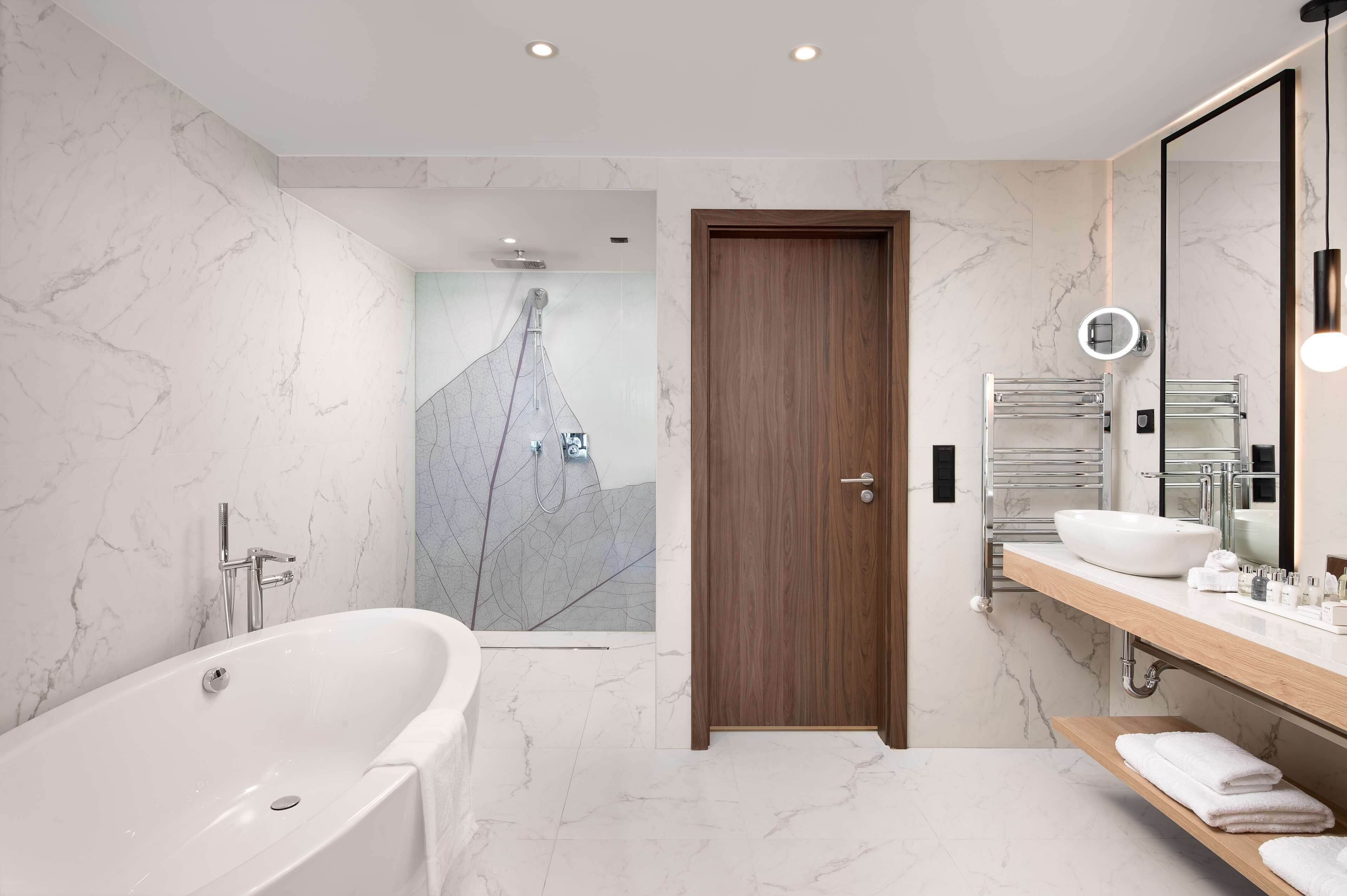 A modern bathroom with a freestanding bathtub, a wooden door, a vanity with a mirror, and a shower area.