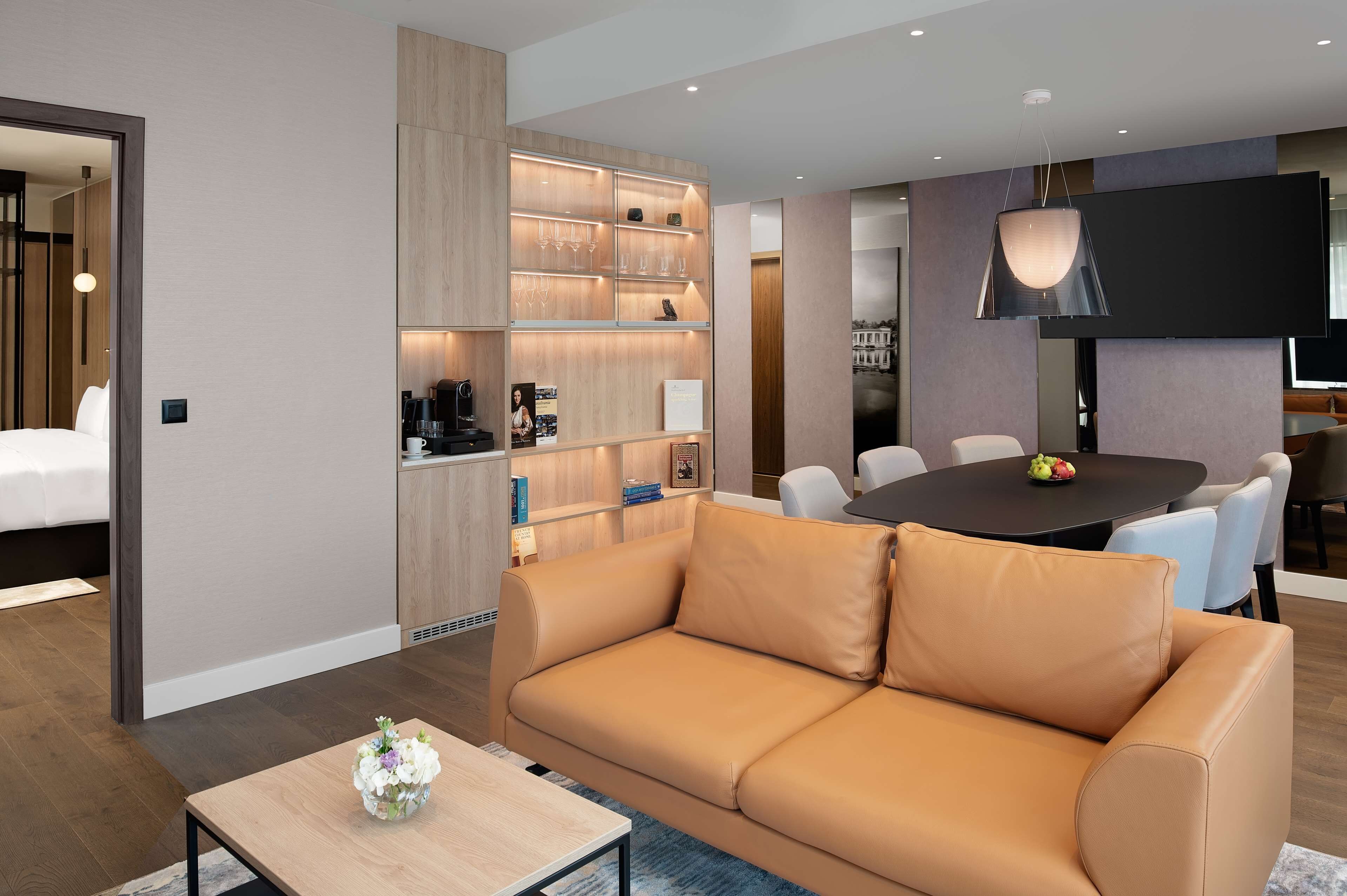 Une chambre d’hôtel moderne équipée d’un canapé, d’une table à manger, d’une télévision et d’un mini-bar.