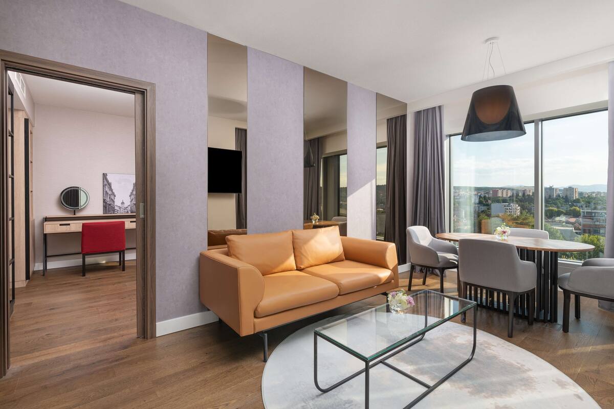 Uma sala de estar moderna com um sofá de couro, uma mesa de centro de vidro e um espaço de jantar com uma mesa redonda e cadeiras.